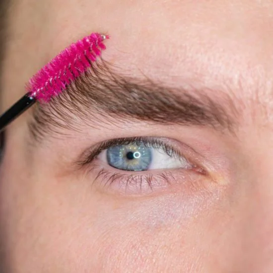 Close-up of a man using a spoolie brush to groom his eyebrows