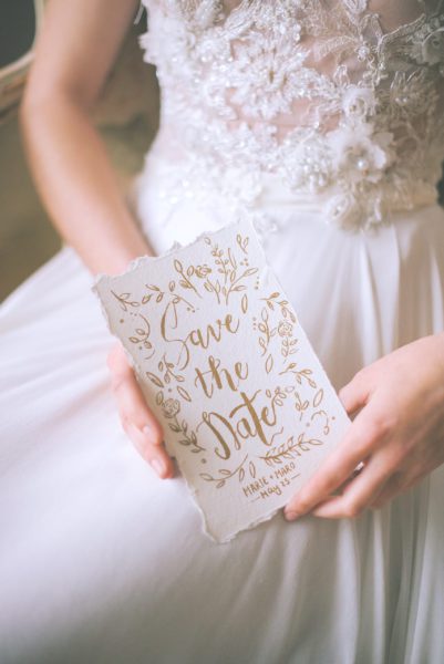 mid-shot of bride in wedding dress holding a save the date card