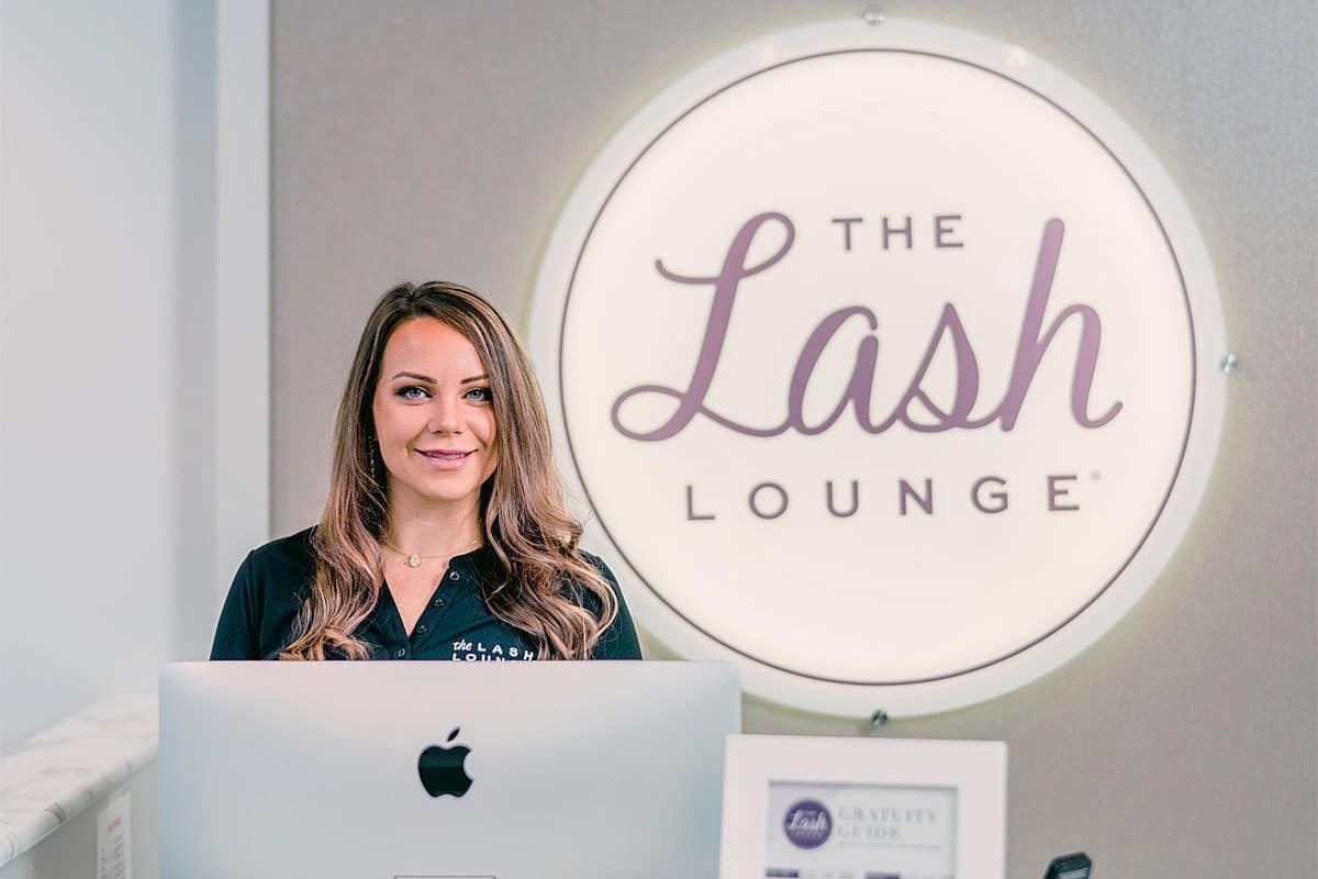 smiling woman standing behind front desk of a Lash Lounge franchise salon