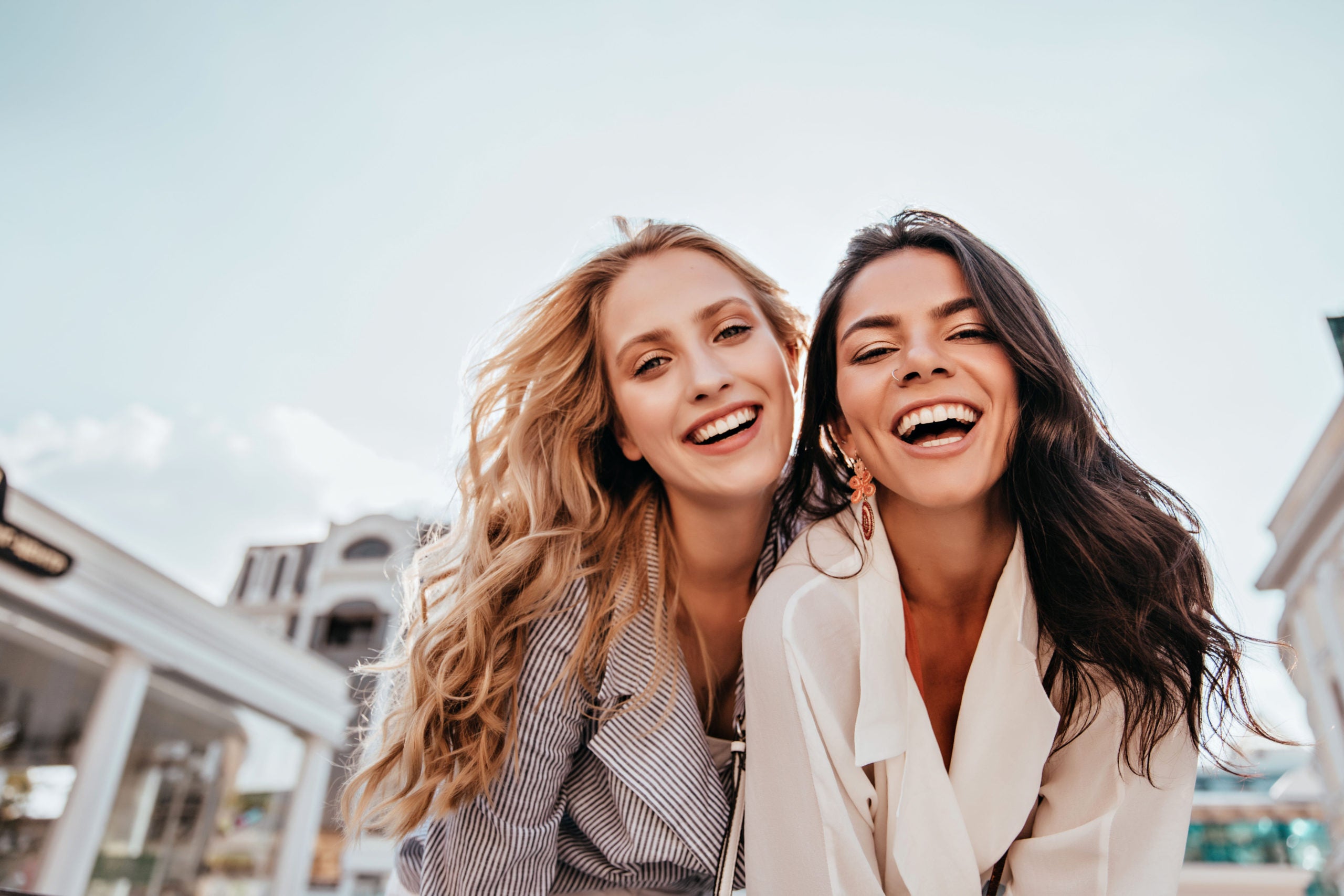 a midshot of two female friends laughing and smiling outdoors in the city