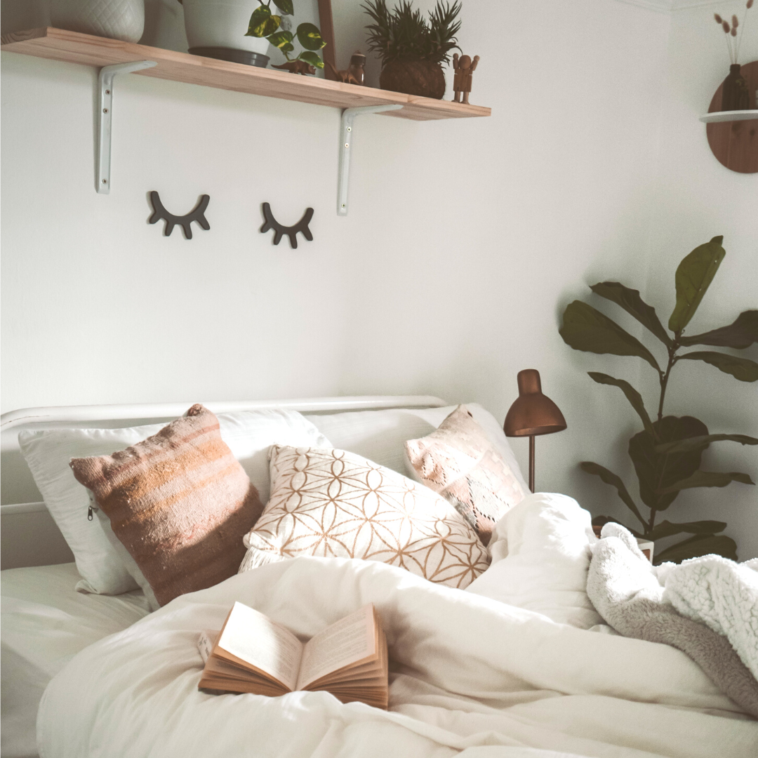 A bedroom with a comfy bed and a shelf above it, plants and eyelash decals on the wall.