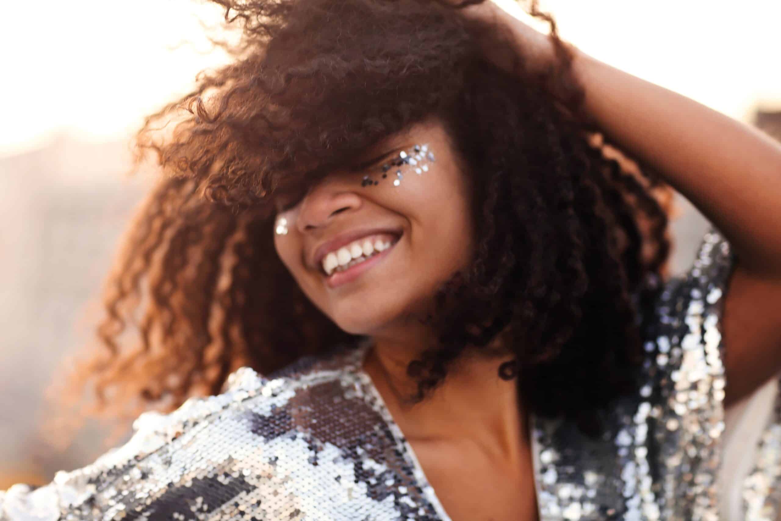 happy black woman smiling in a sparkly dress with bling makeup around eyes