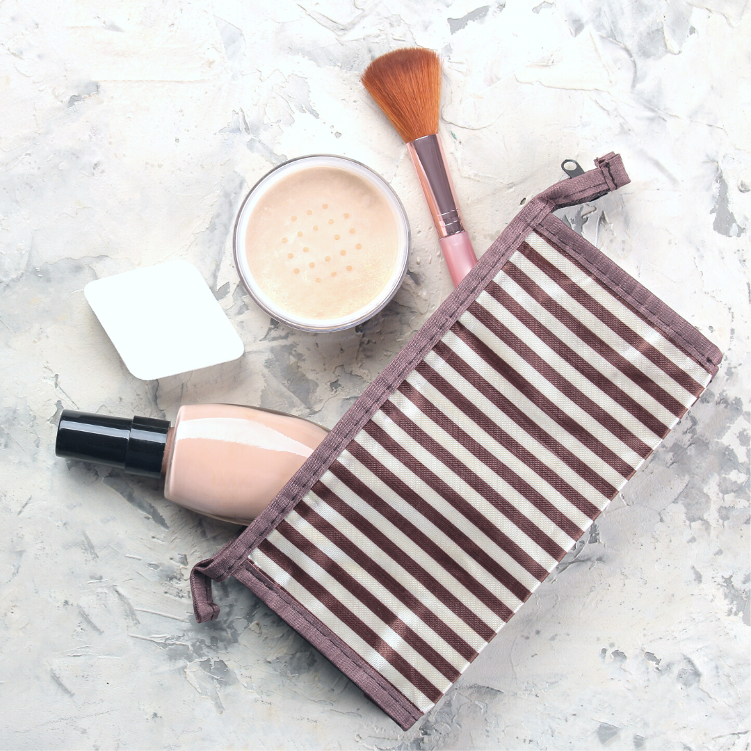A striped makeup bag on marble counter with an array of makeup coming out of bag