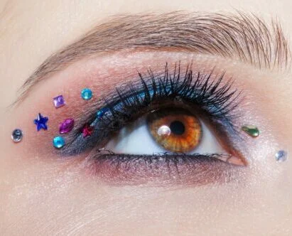 close-up of woman's brown eye with eye makeup and jewels around eye