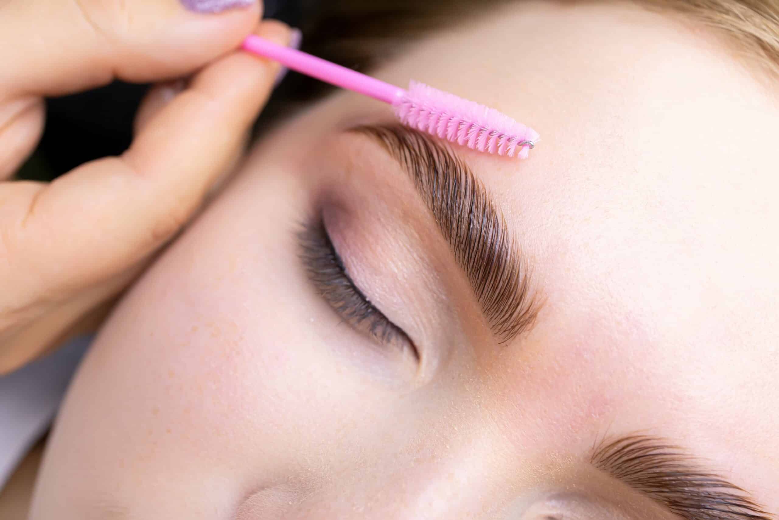 Closeup of woman's eye area as a small brow comb brushes her shaped eyebrow