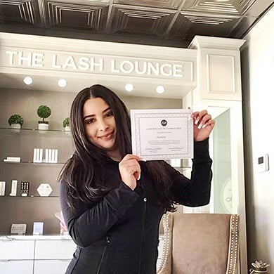 A Lash Lounge stylist smiling and holding her lash tech credentials