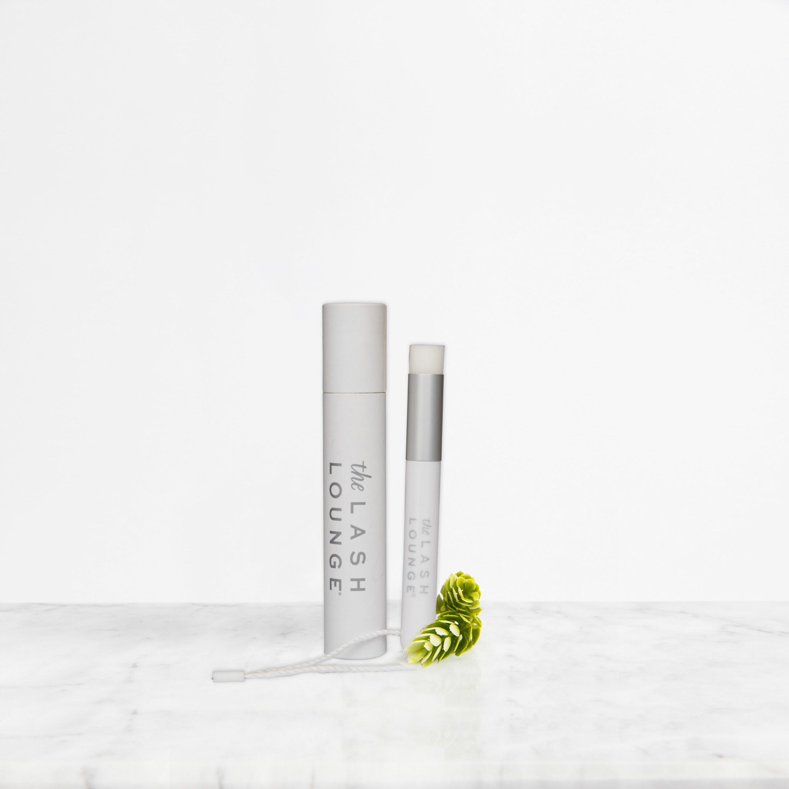 The Lash Lounge's Eyelash Cleansing Brush and Barrel laying down on a marble counter.