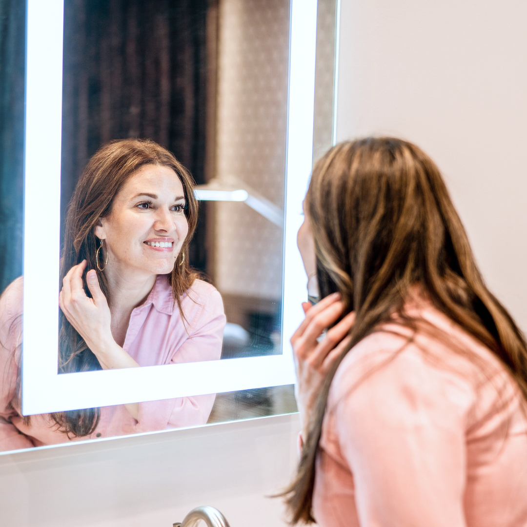 woman leaning in to look in mirror to admire her hair and lash growth