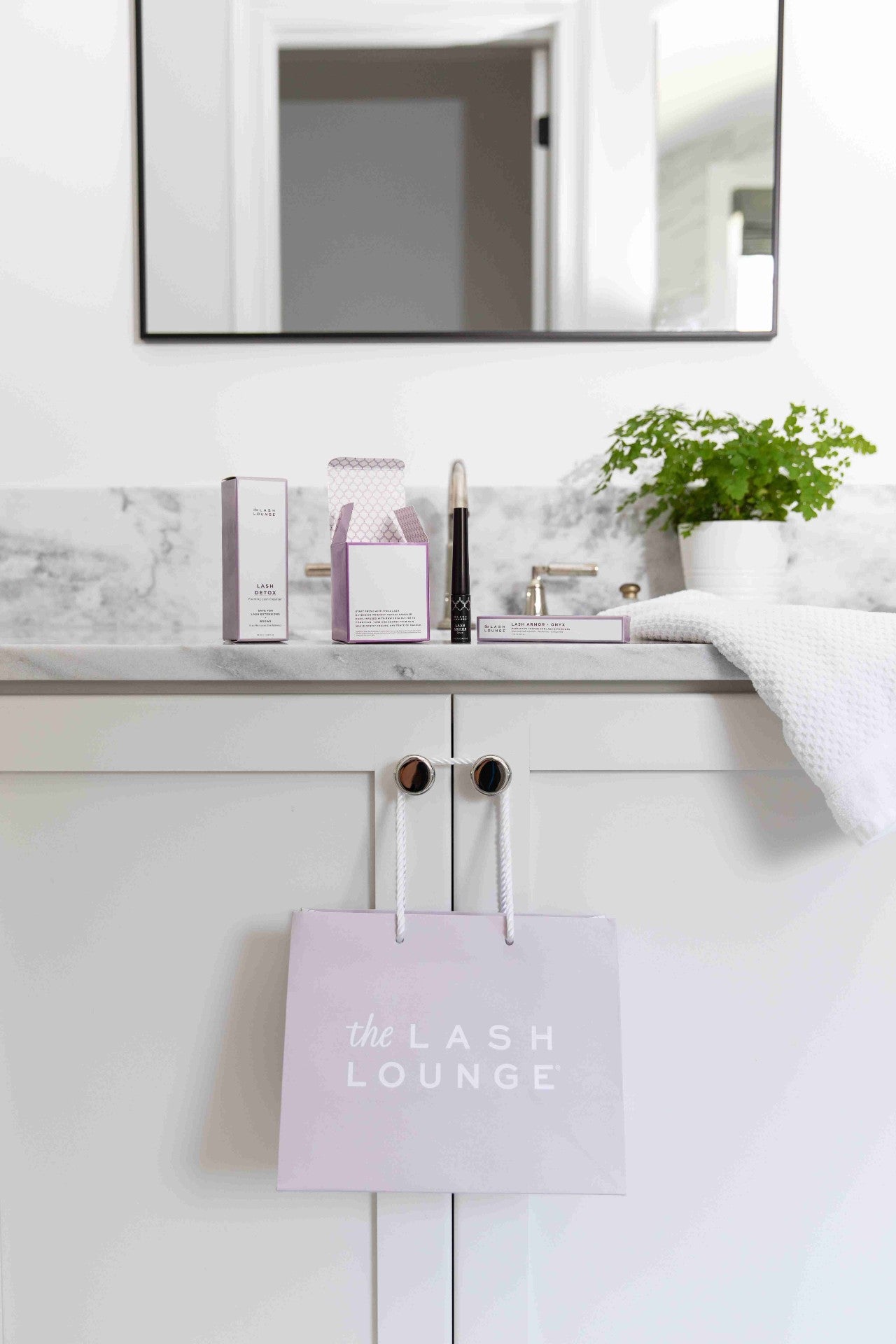 a bathroom counter with Lash Lounge products and bag hanging from cabinet