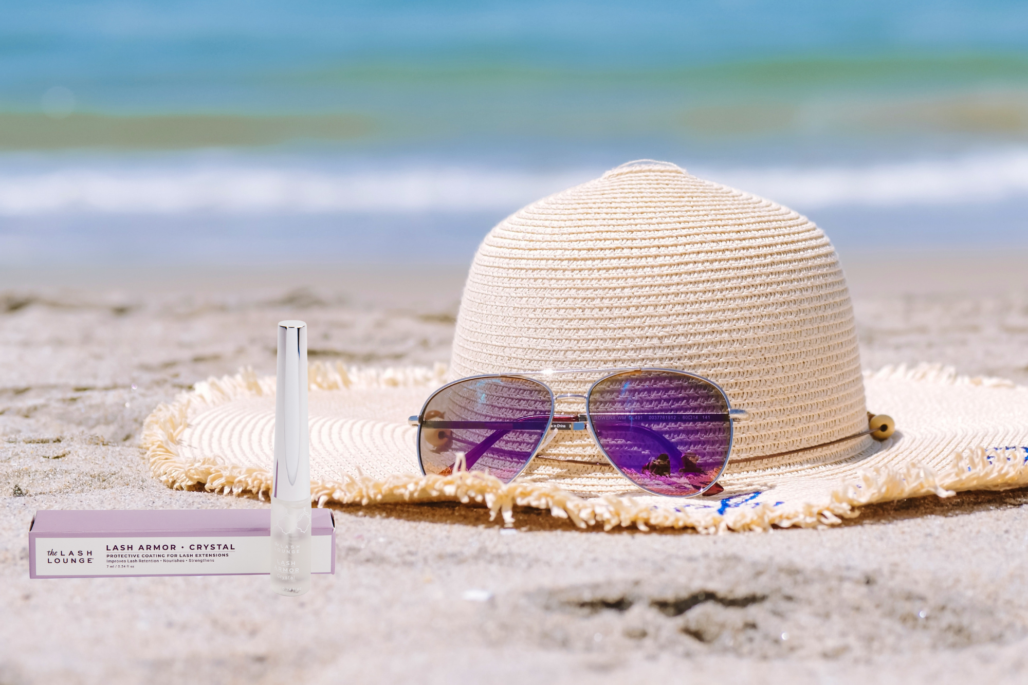 floppy hat, sunglasses and Lash Armor sealant resting on a sandy beach