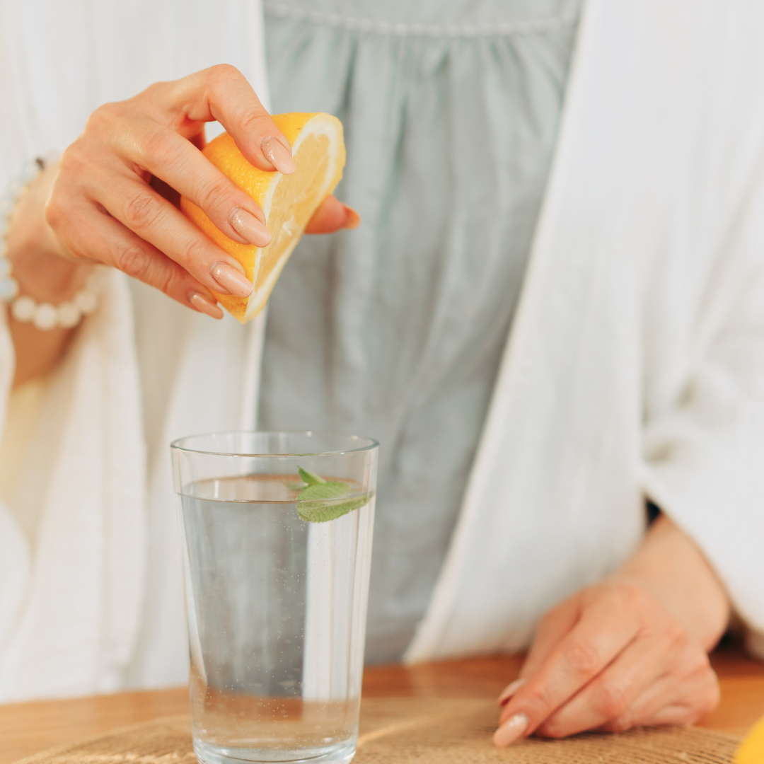 woman's hand squeezing a lemon into a glass of water