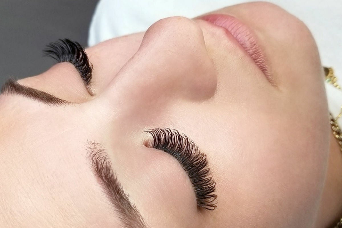 A close-up of a woman lying down with her eyes closed with lash extensions