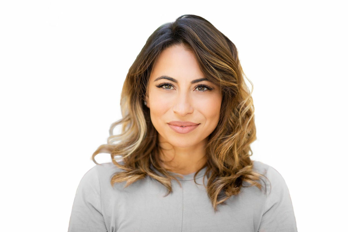 A woman with wavy hair smiling, eyelash extensions, and full eyebrows smiling and facing forward