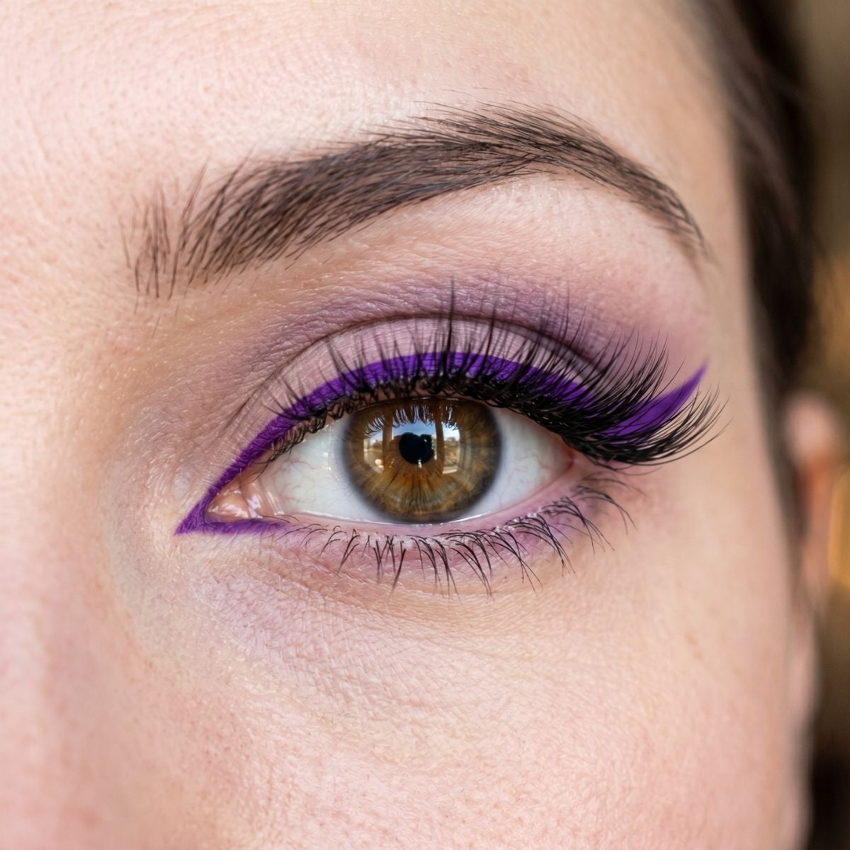 Closeup of eye with graphic purple eyeliner and lash extensions.