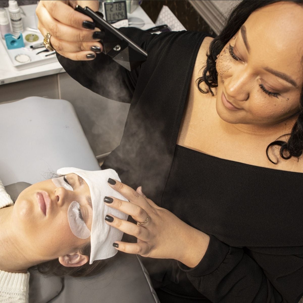 Stylist spraying product onto the face of a guest laying down in lash chair