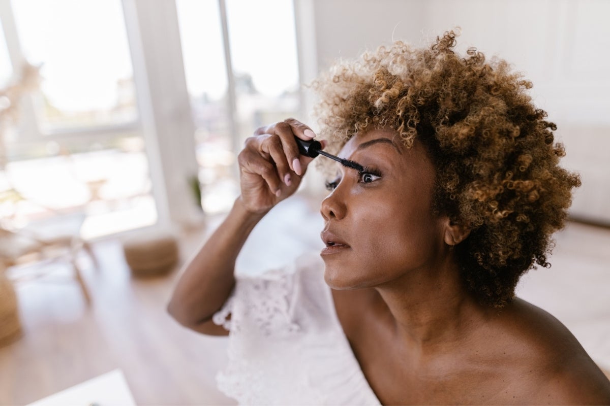 Woman of color applying mascara to her eyelashes.