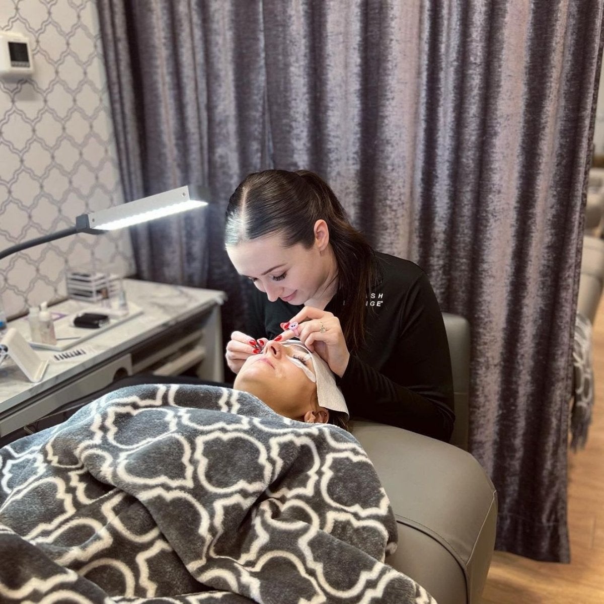 Guest laying in chair and lash stylist applying lash extensions.