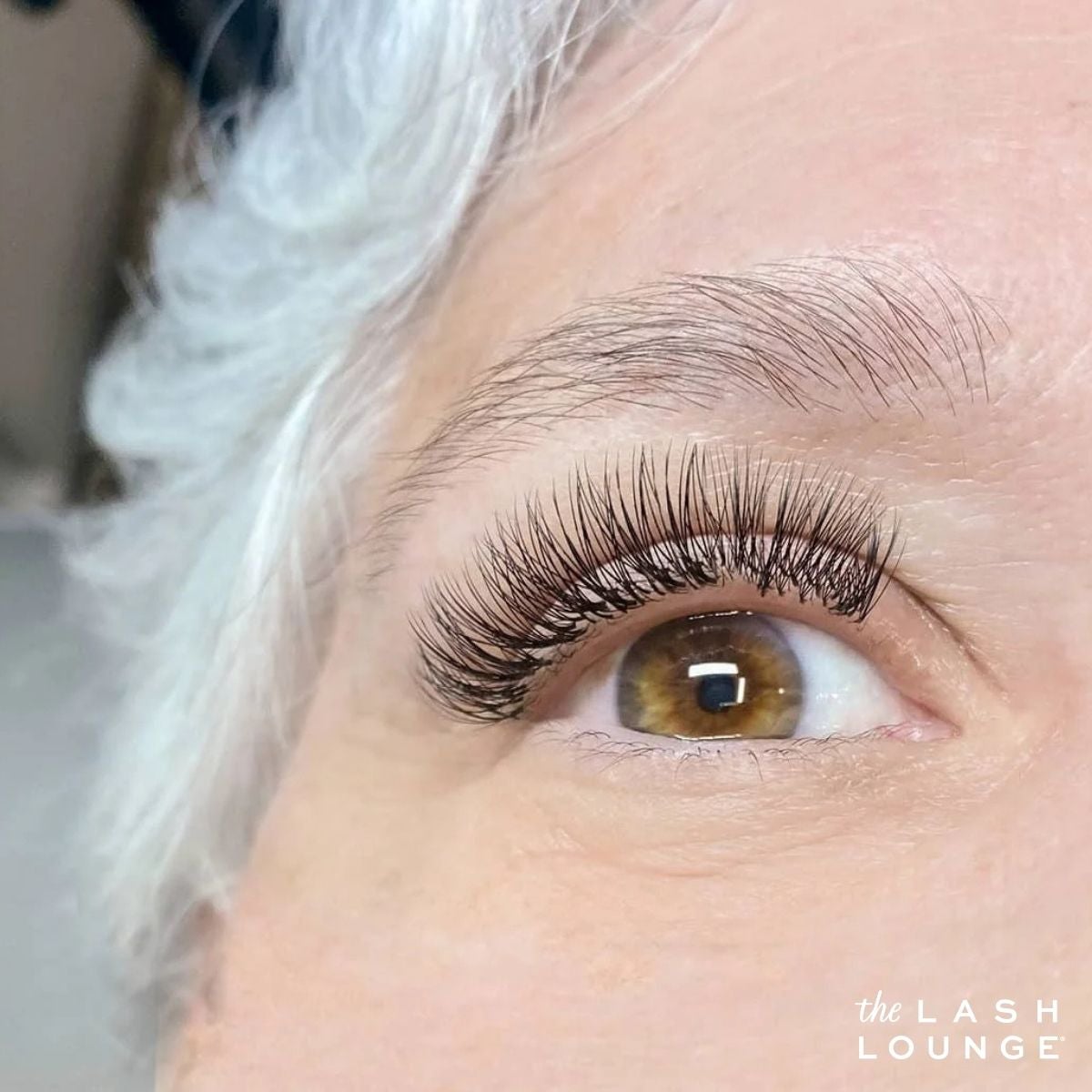 Mature adult woman with grey hair and eyelash extensions and threaded eyebrows from The Lash Lounge.